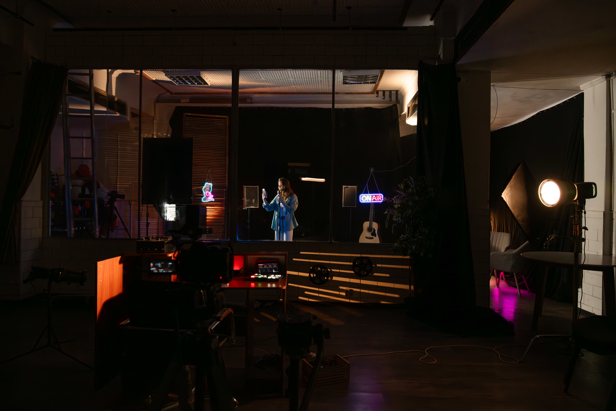 A warmly lit recording studio with an 'ON AIR' sign glowing over microphones and instruments